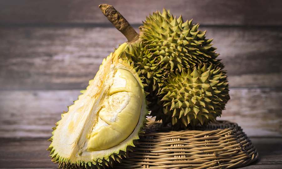 A young durian fruit leaning on a cut piece of durian in a bamboo basket