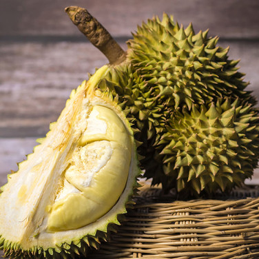 A young durian fruit leaning on a cut piece of durian in a bamboo basket