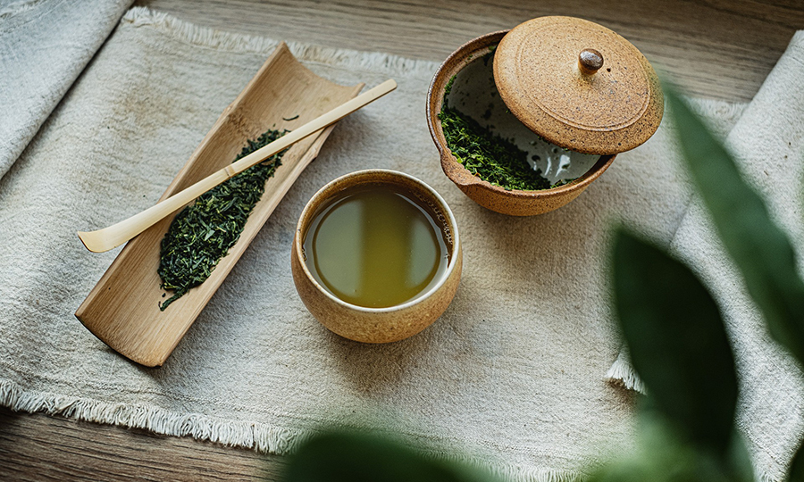 A cup of freshly brewed green tea from a traditional tea brewing set plated on a woven fabric