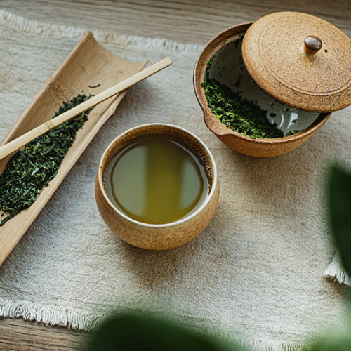 A cup of freshly brewed green tea from a traditional tea brewing set plated on a woven fabric