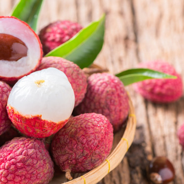 wooden bowl of ripe lychees with 2 cut open lychees on top