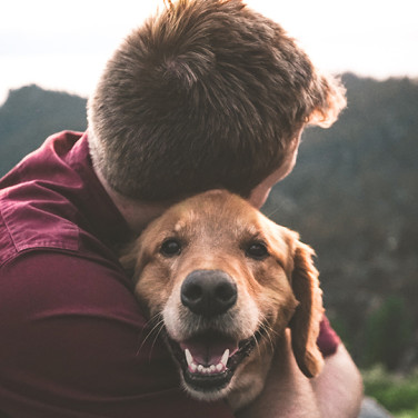 Man hugging tan dog outdoors