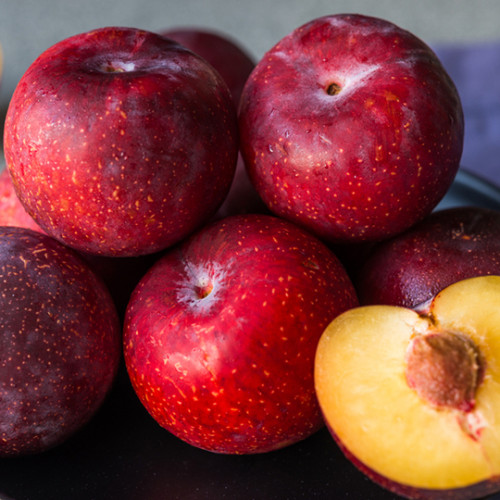 ripe plums on ceramic dish with single peach cut half open