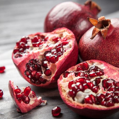 open halves of pomegranate next to two pomegranates on wooden cutting board