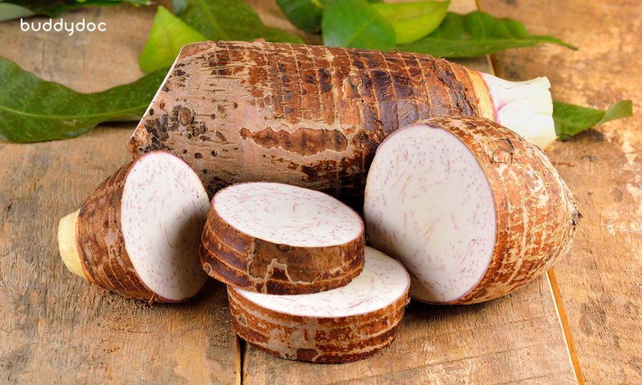 sliced chunks of taro root in front of whole taro root on wooden table