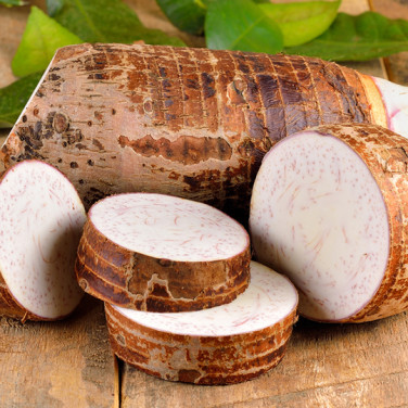 sliced chunks of taro root in front of whole taro root on wooden table