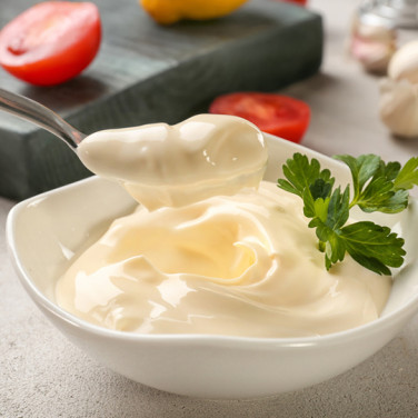 spoonful of mayonnaise in front of bowl of mayonnaise next to fresh ingredients