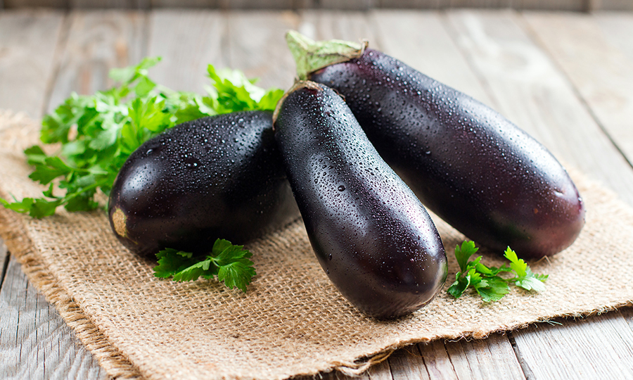 Three eggplants laid on top of a woven fabric