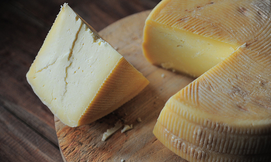 A wheel cheese with a chunk cut out of it laid on a wooden surface