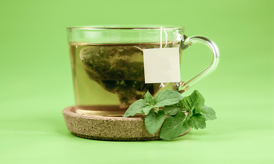 A glass cup of hot water steeping a green tea bag on a stone coaster