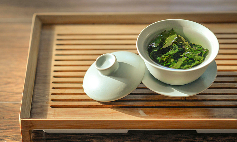 A cup of brewing green tea in a clay tea pot set on a wooden tray