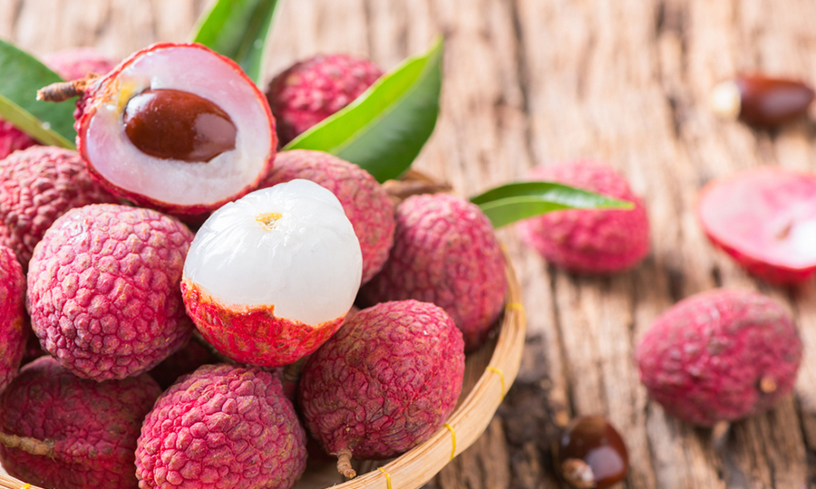 wooden bowl of ripe lychees with 2 cut open lychees on top
