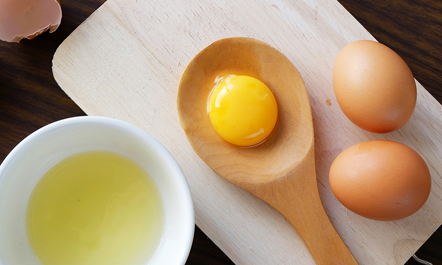 Raw egg yolk separated from the egg white in a wooden spoon