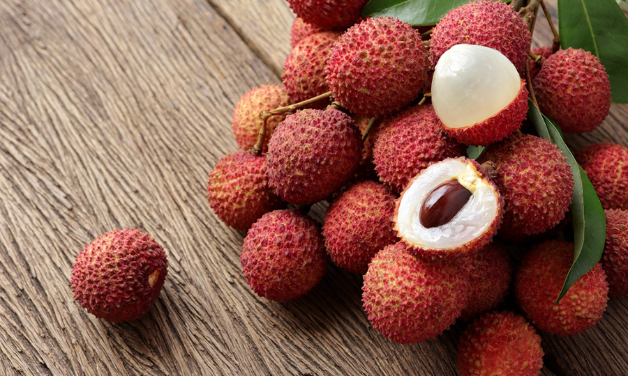 lychees on wooden table with two open lychees showing white flesh inside