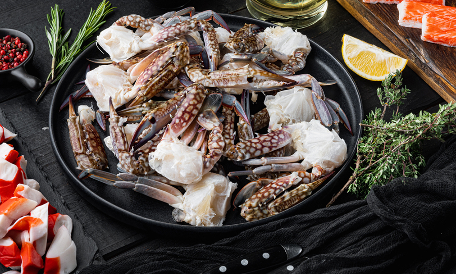 raw crab halves in black dish surrounded by imitation crab and spices