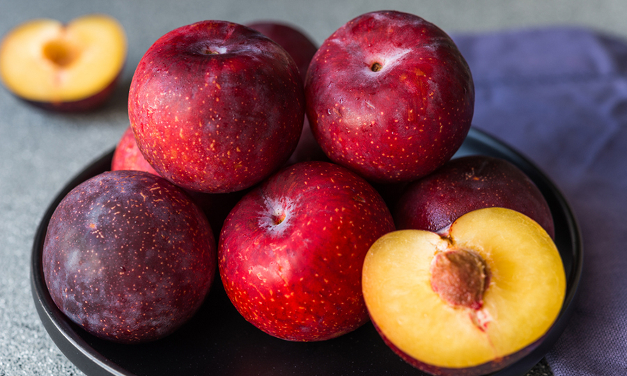 ripe plums on ceramic dish with single peach cut half open