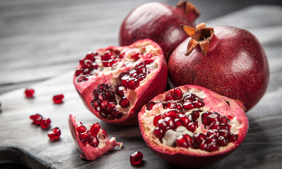 open halves of pomegranate next to two pomegranates on wooden cutting board