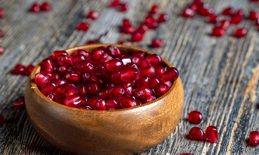 wooden bowl of pomegranate seeds with more seeds scattered around the bowl