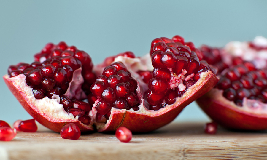 close up of open pomegranate and its seeds on wooden table