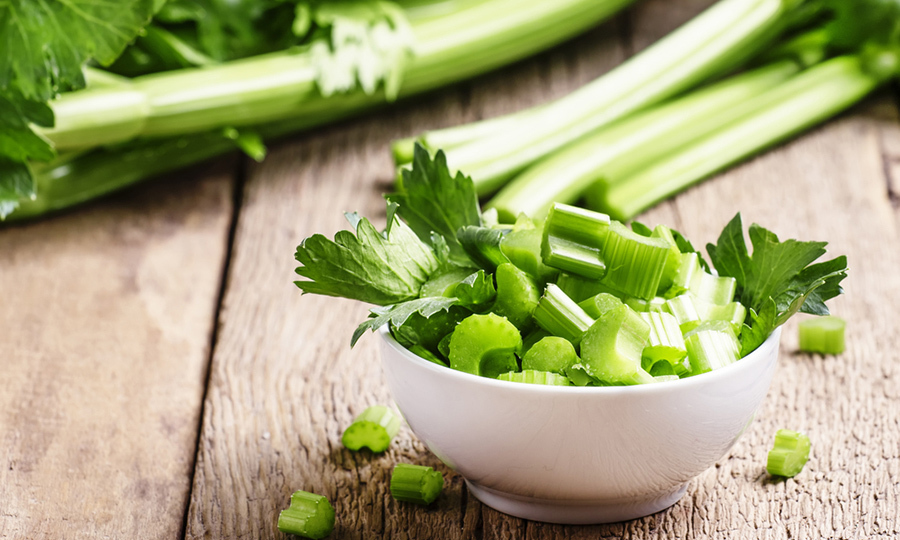 bowl of cut up celery on wooden table with celery sticks in the background