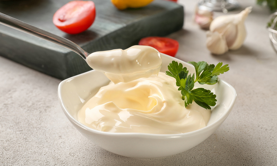 spoonful of mayonnaise in front of bowl of mayonnaise next to fresh ingredients