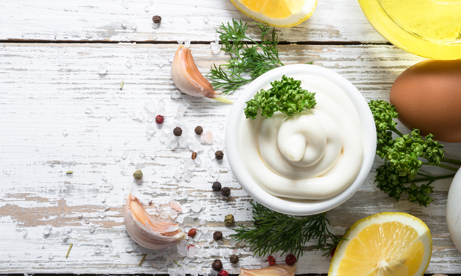 bowl of mayonnaise with seasoning and fresh ingredients next to it