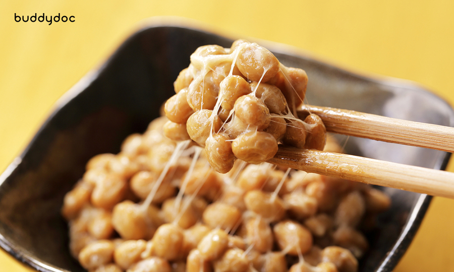 close up of natto between wooden chopsticks from black bowl