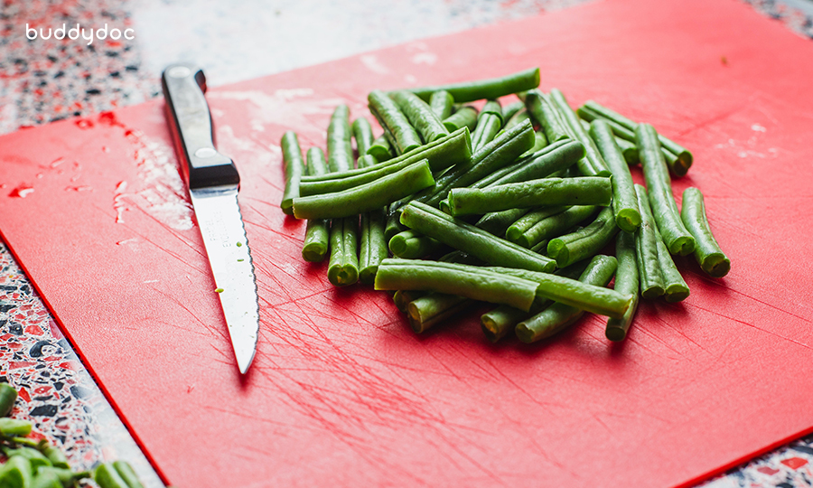 pile of sliced green beans next to knife on red cutting board