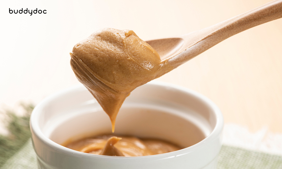wooden spoonful of creamy peanut butter from white ceramic bowl