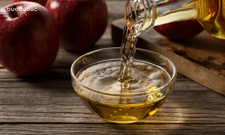 apple cider vinegar poured into small glass ramekin with two red apples in the background