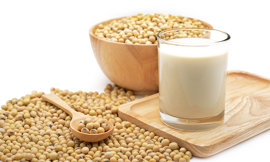 glass of soy milk next to bowl of soybeans and spoonful of soybeans