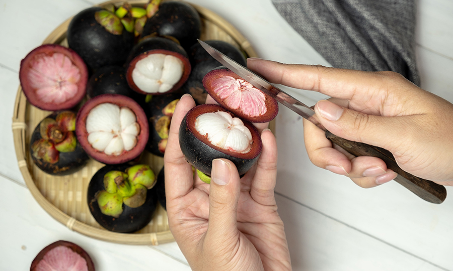 A southeast asian cutting open several mangosteen fruits in a bamboo tray